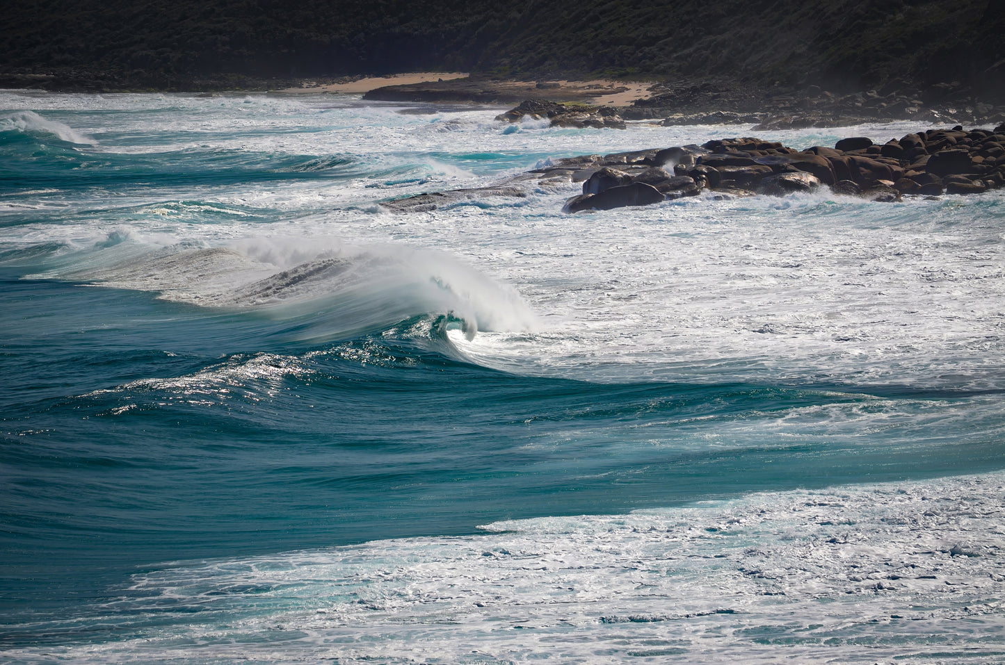 Deep-blue swell rising before breaking onto rock ledges and shelves.