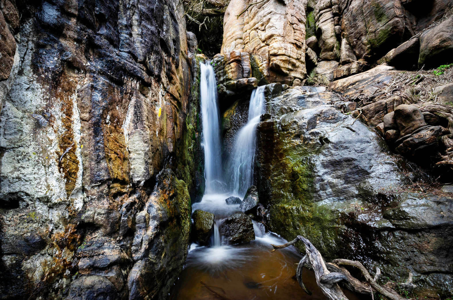 Secluded waterfall cascading down rocky cliffs with moss and greenery