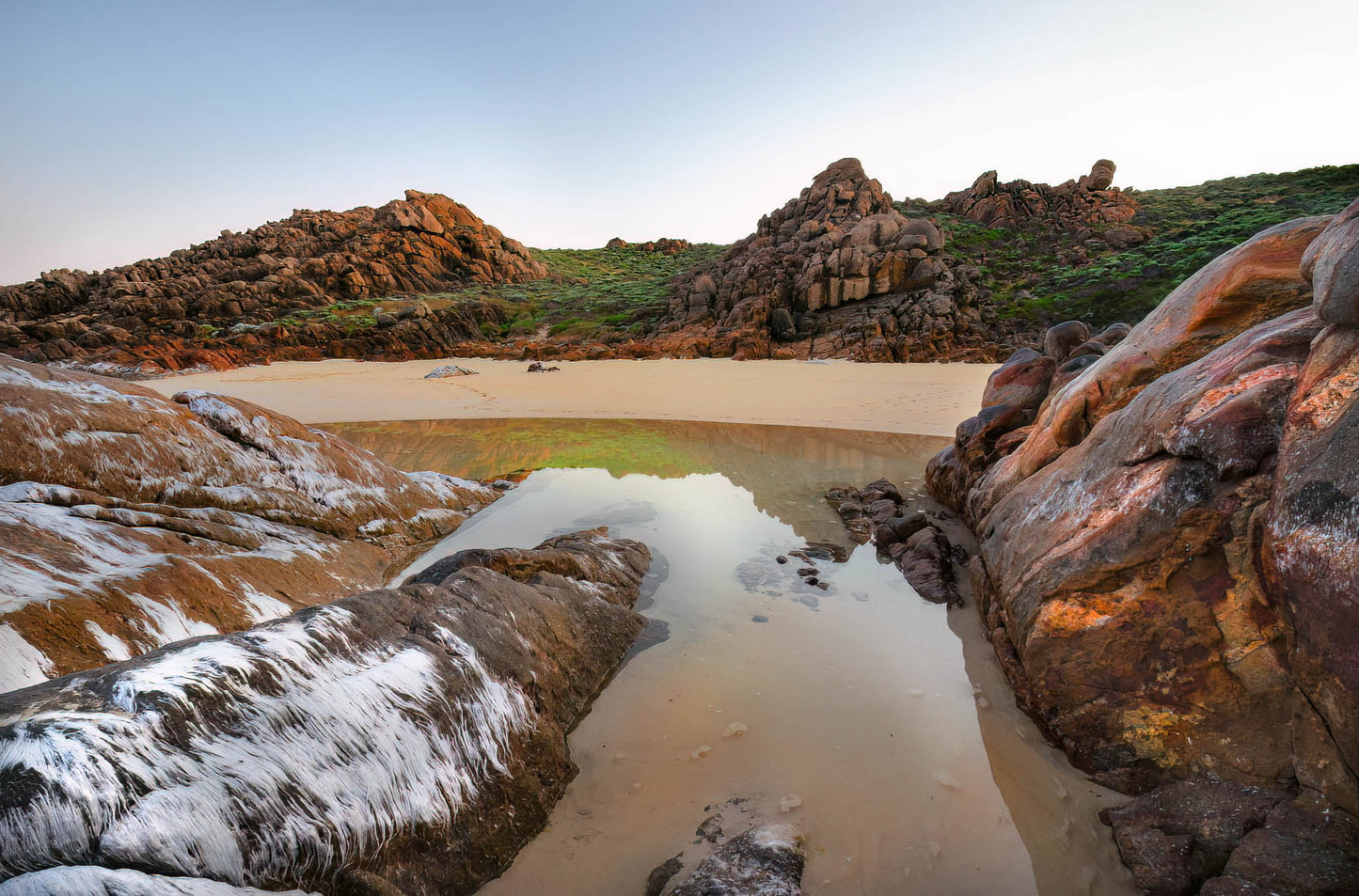 Rugged coastal landscape with rocks and a small reflective pool of water.