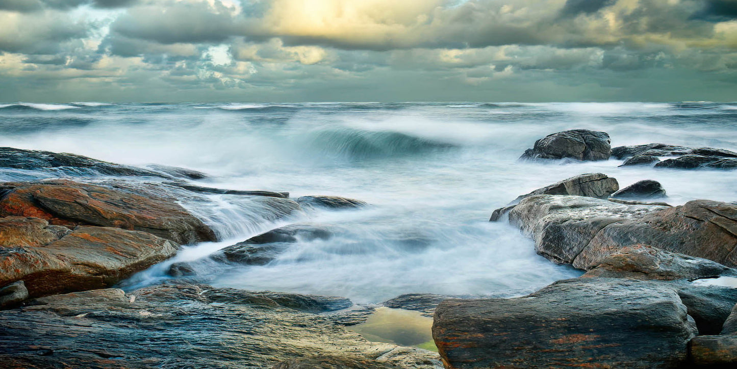 Raging ocean waves crashing against rocks with a stormy sky.