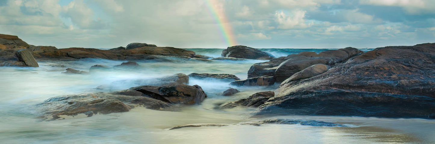 Rocks by the ocean with a rainbow in the background at Redgate Beach.