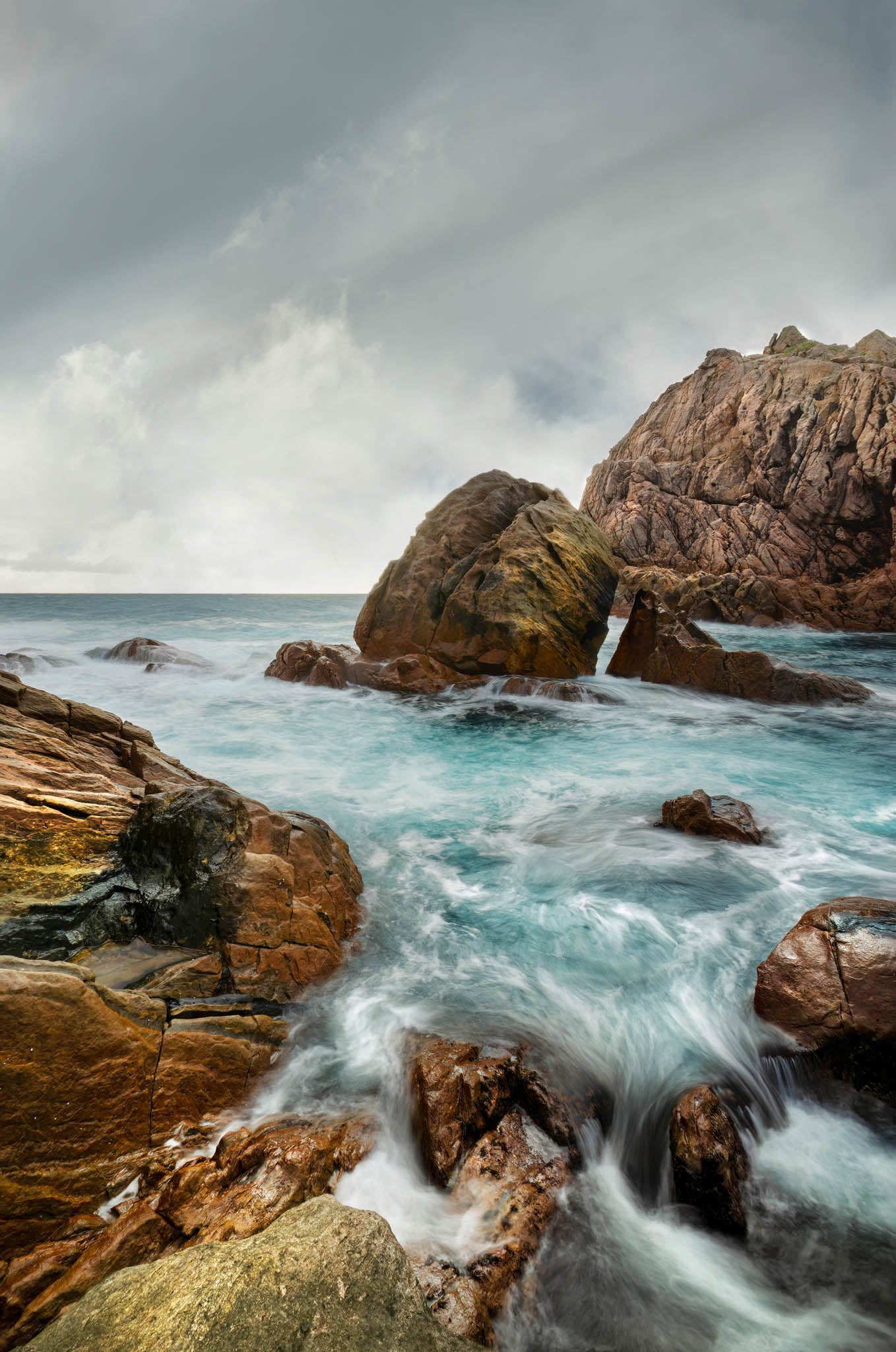 Long-exposure seascape at Sugarloaf Rock with glistening rocks in the foreground.
