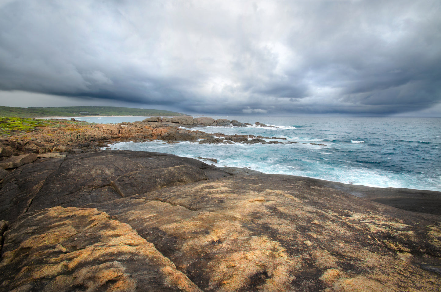 Dramatic storm surge forming under low, brooding clouds with rain falling in the distance at Yallingup.