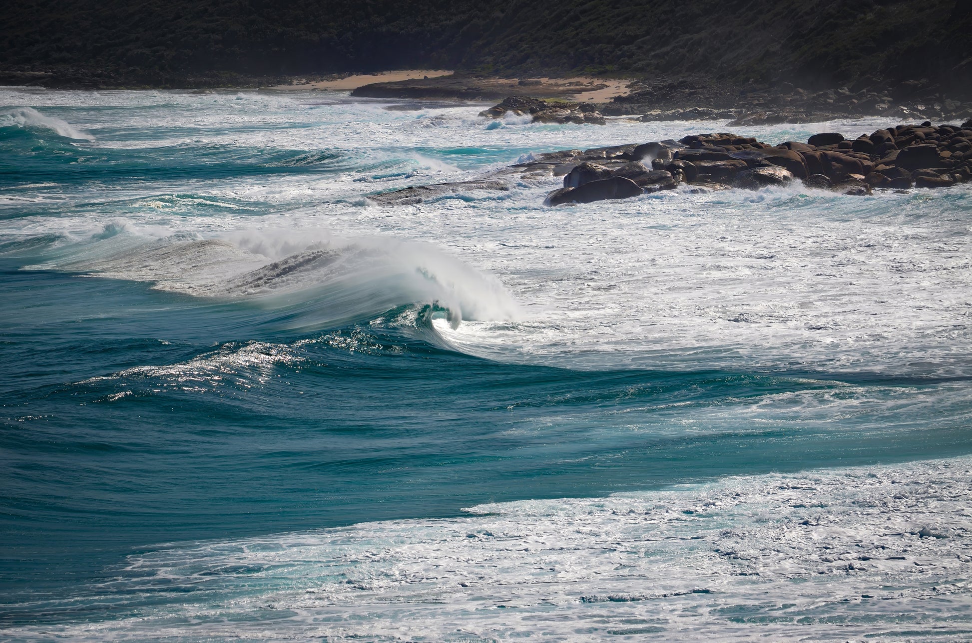 Deep-blue swell rising before breaking onto rock ledges and shelves.