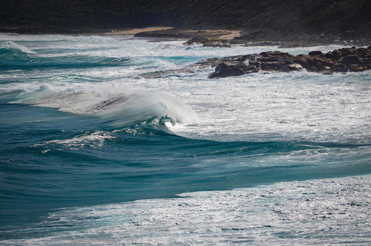 Deep-blue swell rising before breaking onto rock ledges and shelves.