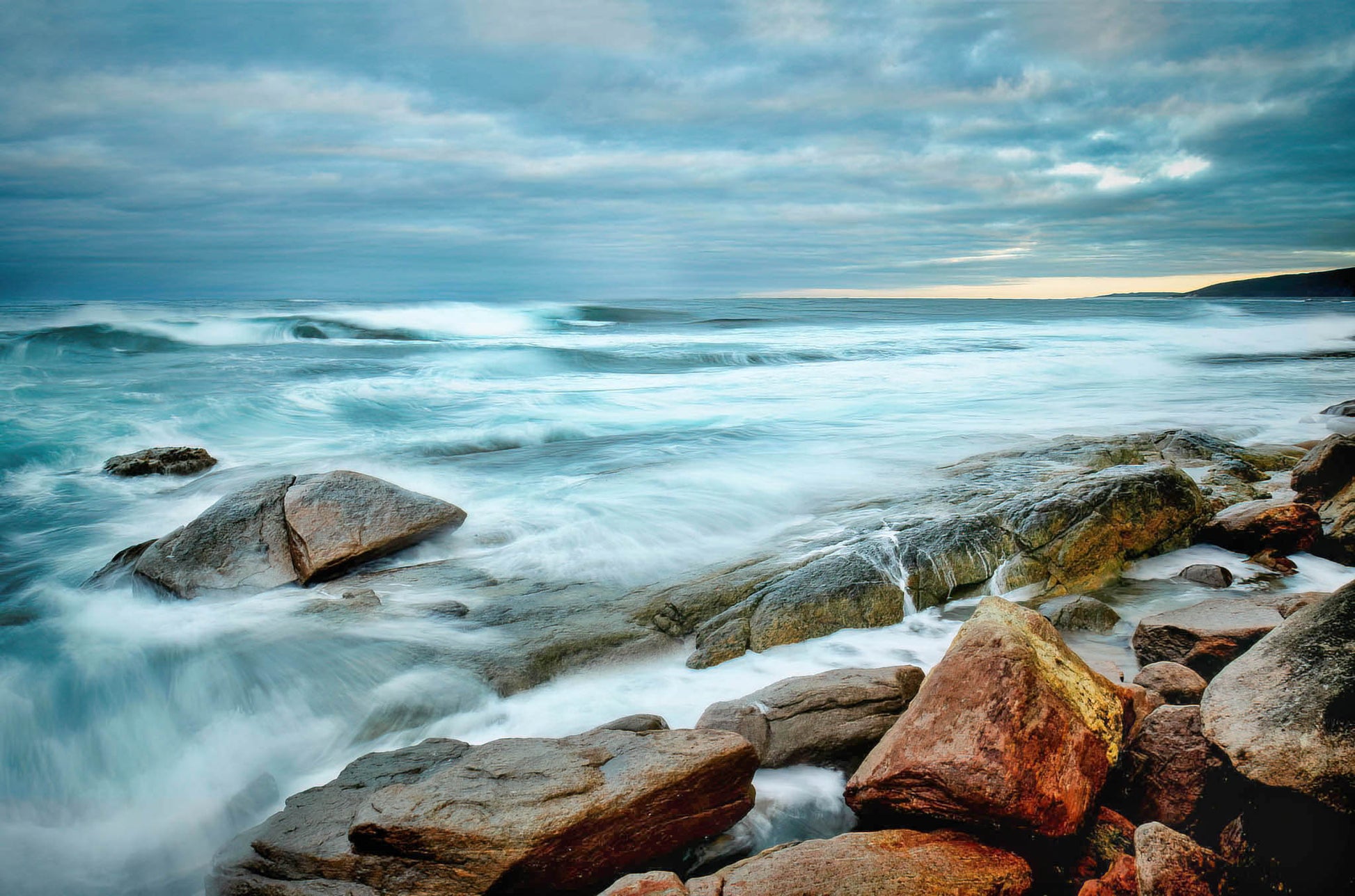 Rocks on a rocky shore with ocean waves and a cloudy sky.