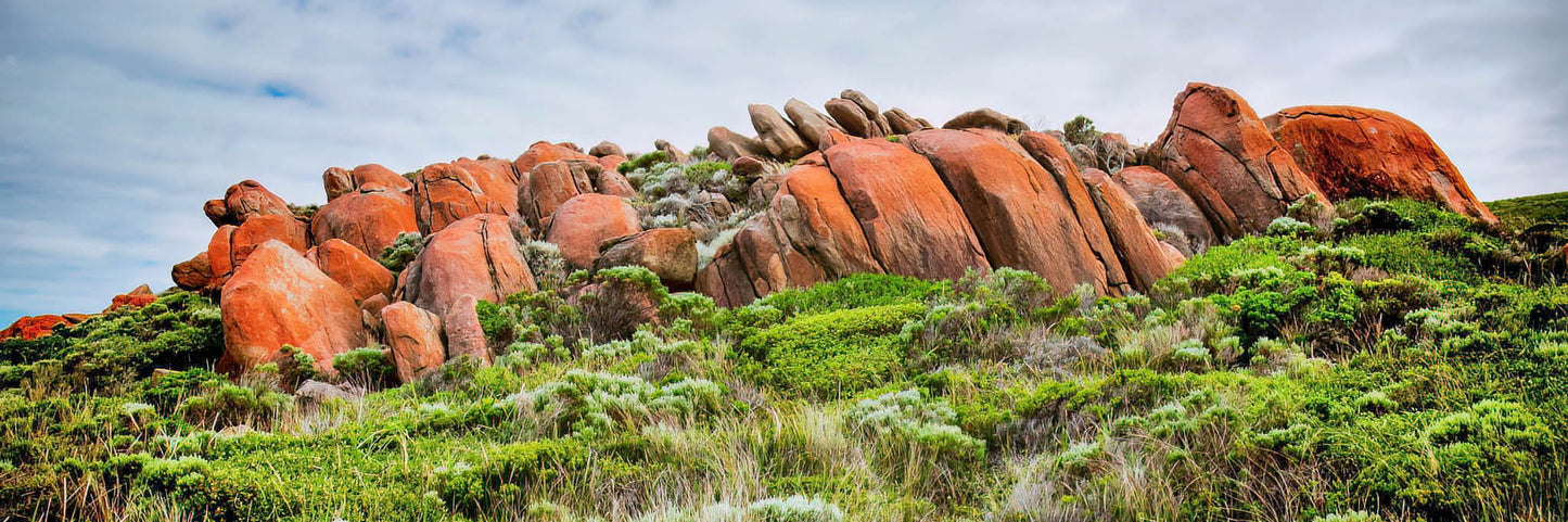 Red rock formations on a grassy hillside with a cloudy sky.