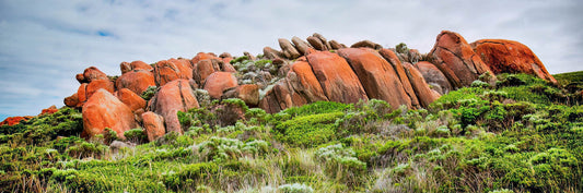 Red rock formations on a grassy hillside with a cloudy sky.