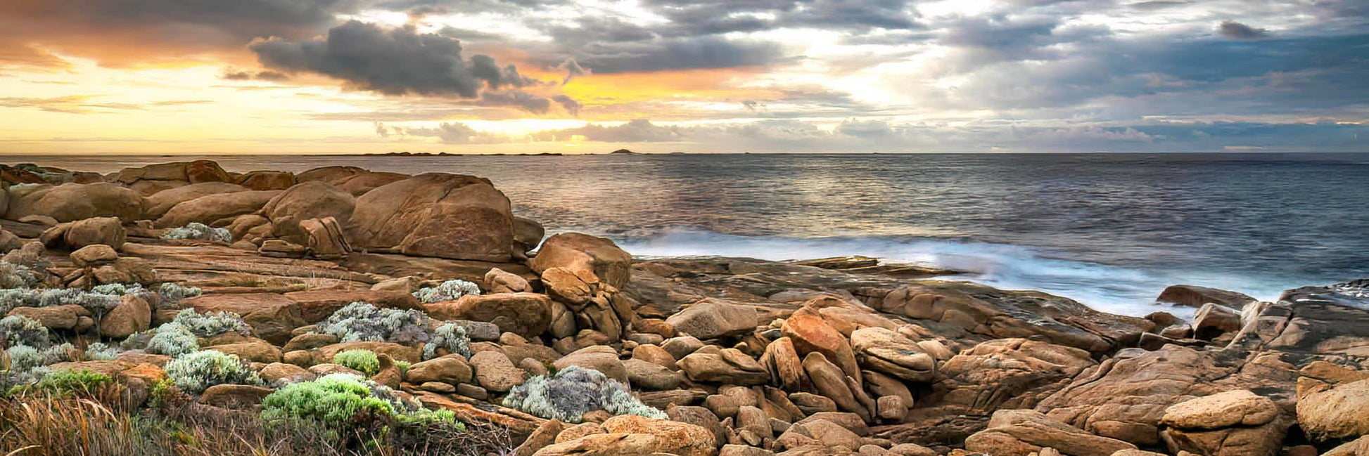 Rocks on a beach at dawn with ocean and sunrise in the background