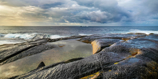 Rocks on a beach with ocean waves and cloudy sky