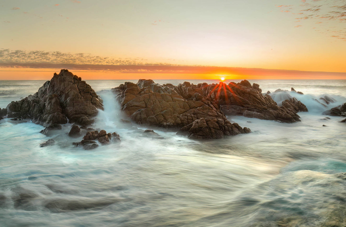 Sunset over rocky coastline with waves crashing against the rocks.