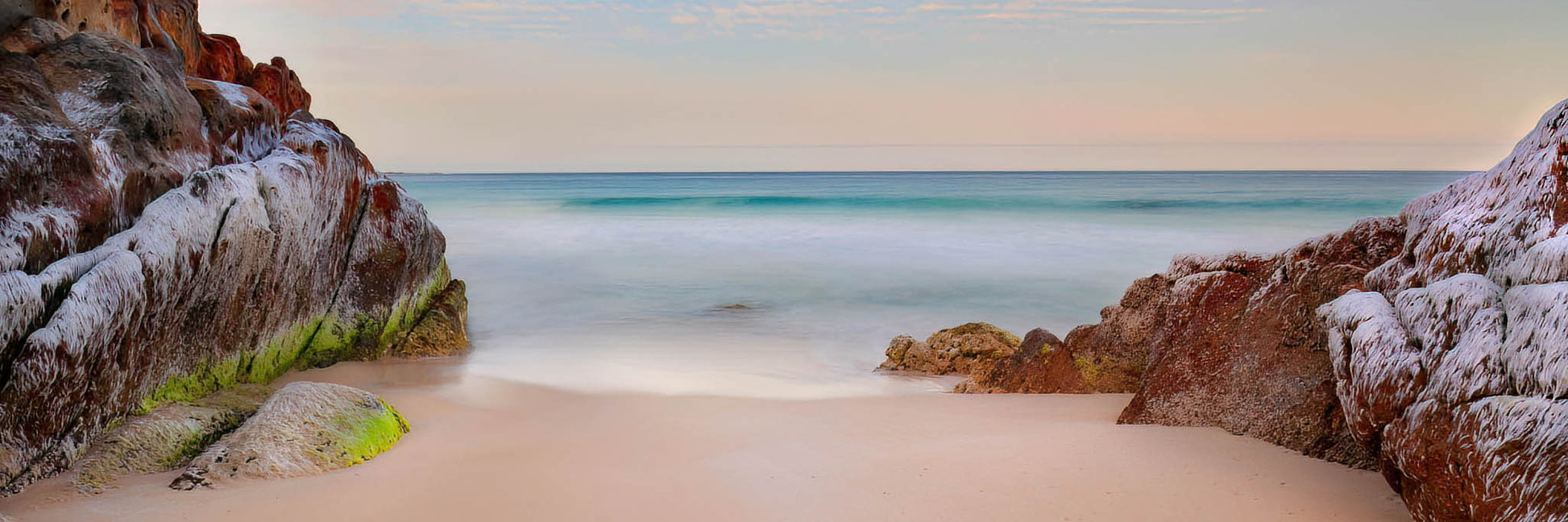 Panoramic view of a beach with rocky cliffs and a clear sky.