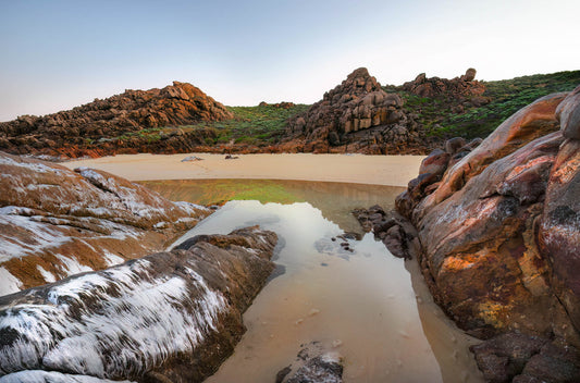 Rugged coastal landscape with rocks and a small reflective pool of water.
