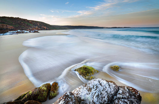 long exposure of tide washing in on beach and around rocks