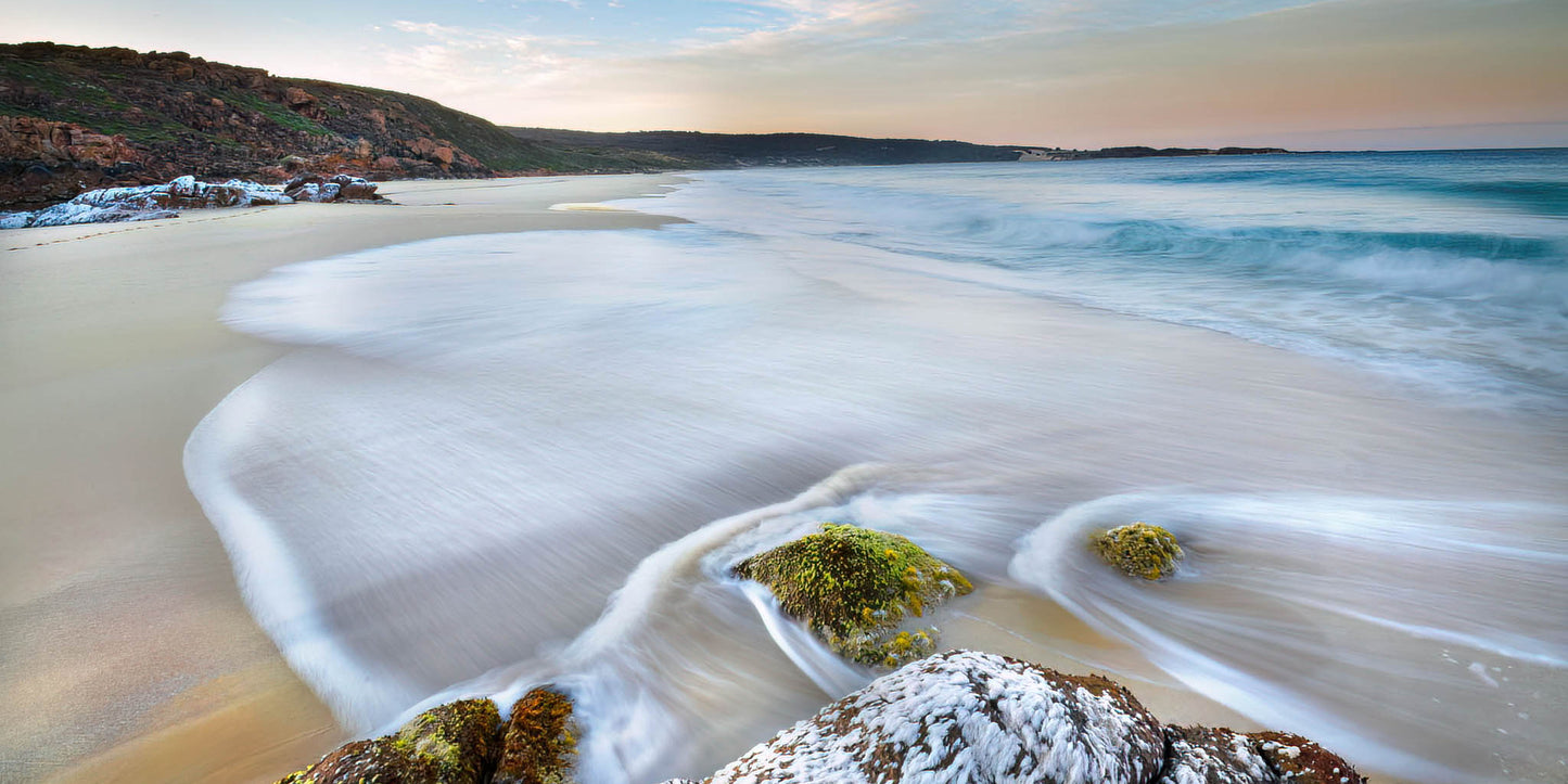 Beach scene with waves and rocks at sunrise