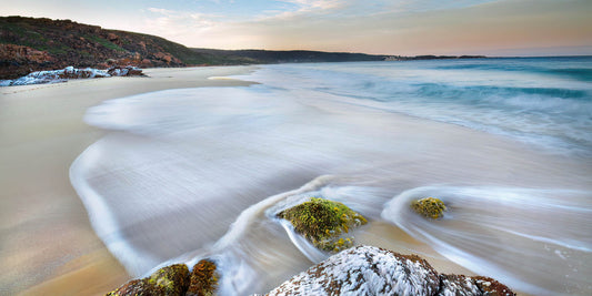 Beach scene with waves and rocks at sunrise