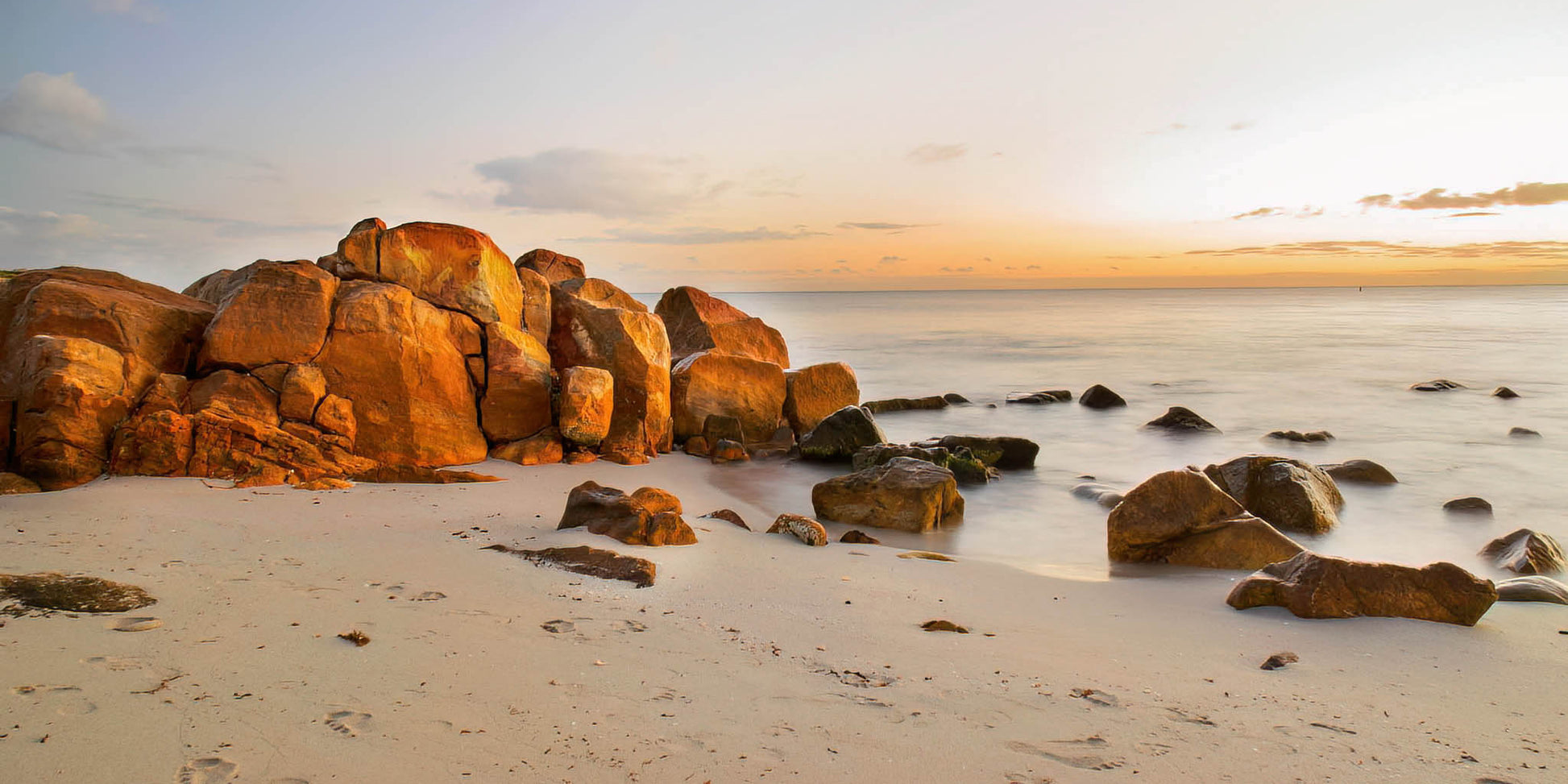 Rocks on a sandy beach with a golden sunrise sky