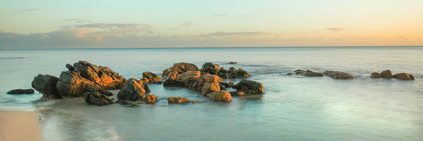 Rocks on a beach during sunrise with a calm ocean.