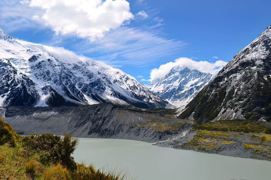 Mountain landscape with a lake and snow-capped peaks under a blue sky.