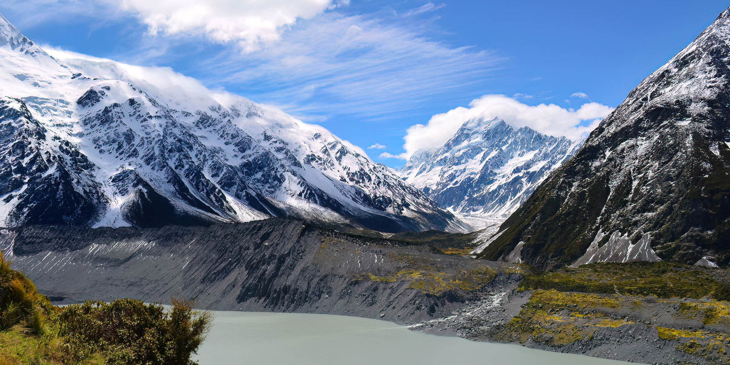 Snow-capped mountains with a lake in the foreground under a blue sky.
