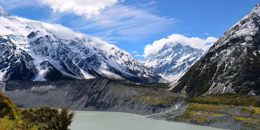 Snow-capped mountains with a lake in the foreground under a blue sky.