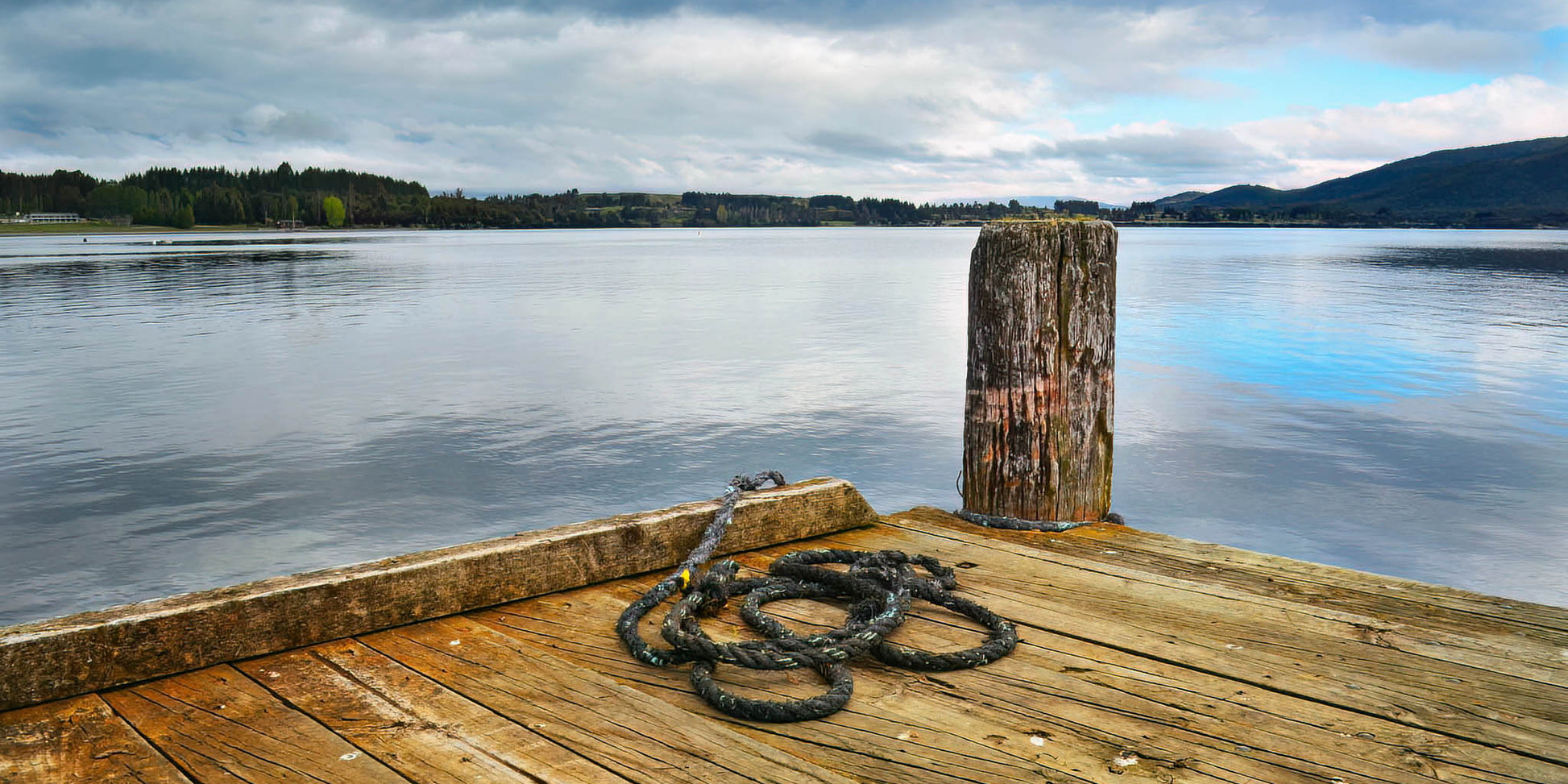 Wooden dock with a rope tied to a post, extending into a calm lake with mountains in the background.