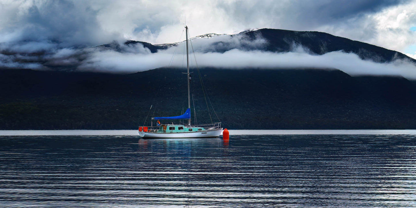 Yacht on a lake with long white clouds above.