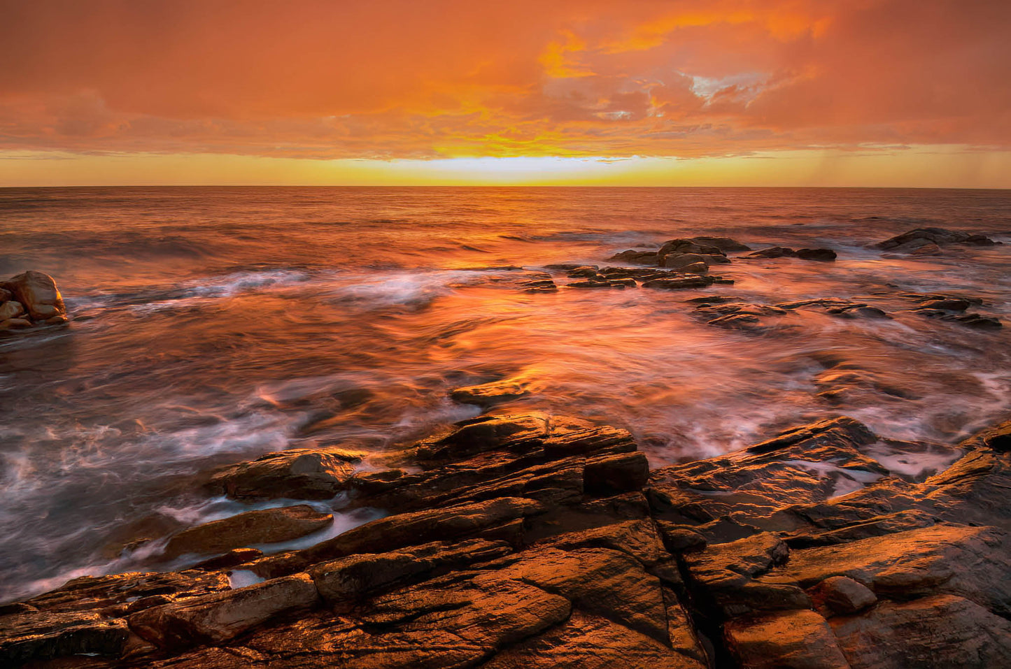 Sunrise over a rocky coastline with orange and pink hues and stormy sky.