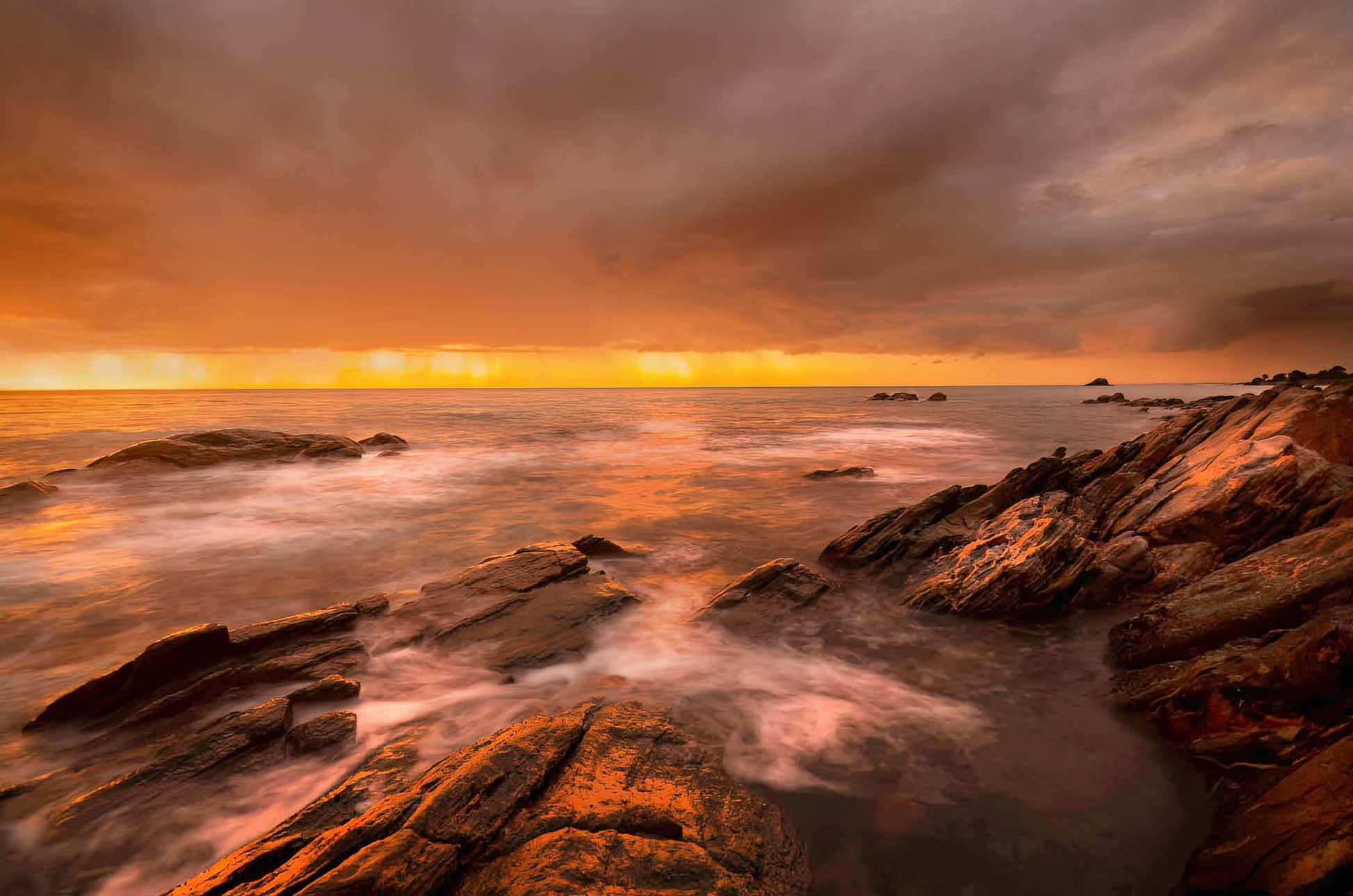 Sunrise over a rocky coastline with warm colors and long exposure effects.