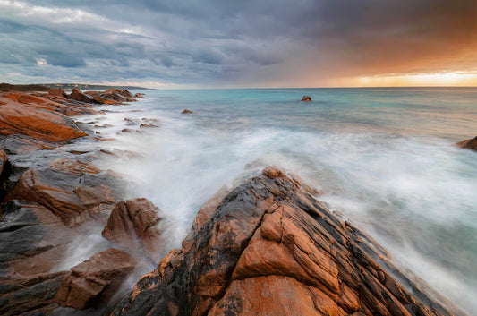 Rugged coastline with waves crashing against rocks under a dramatic sky.