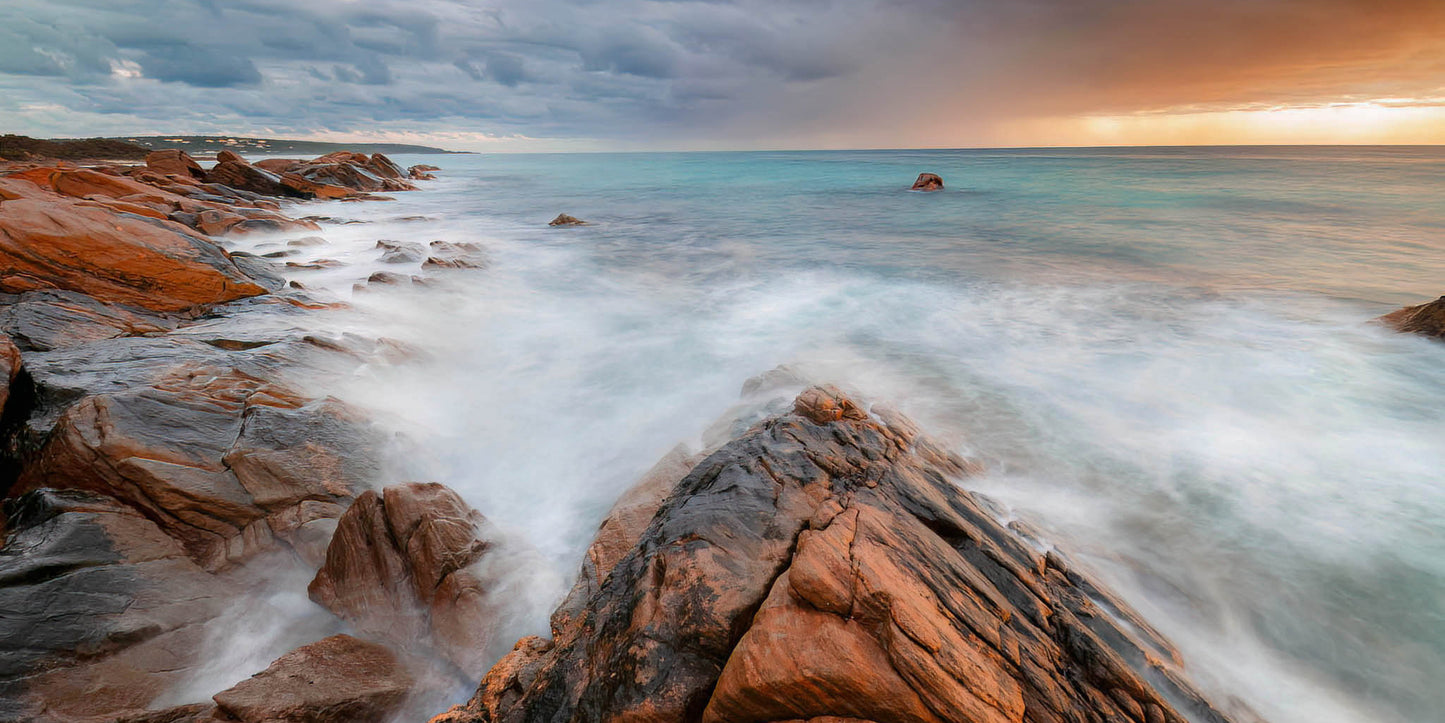 Rugged coastline with waves crashing against rocks during a storm at dawn.