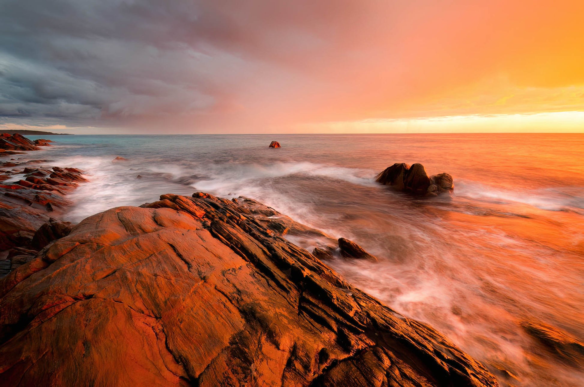 Sunrise over a rocky coastline with warm orange glow and long exposure effect.