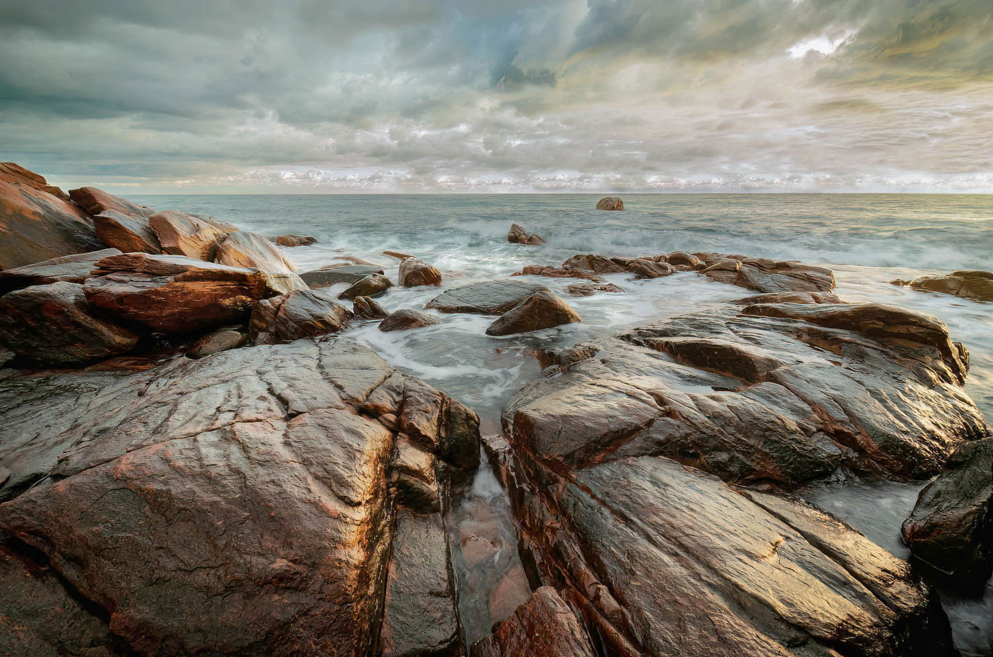 Rocks on a beach with a stormy sky and ocean.