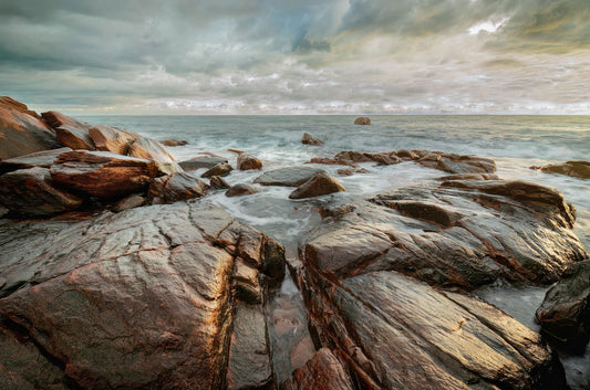 Rocks on a beach with a stormy sky and ocean.