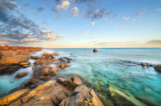 Rocks by the ocean with a clear blue sky and sunrise.