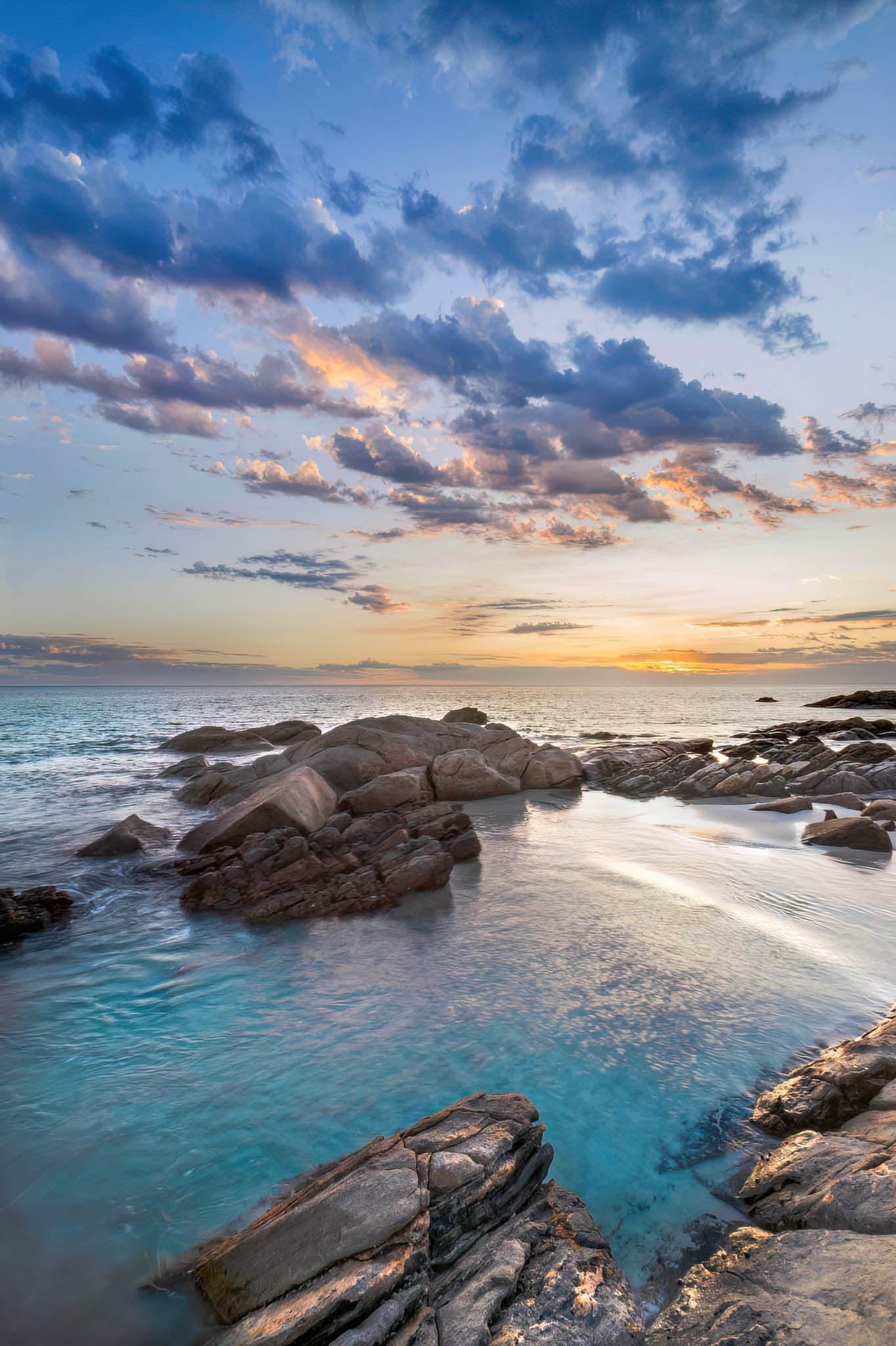 Dawn and sunrise over a rocky coastline with clear blue water.