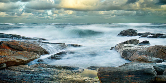 Raging ocean waves crashing against rocks with a stormy sky.