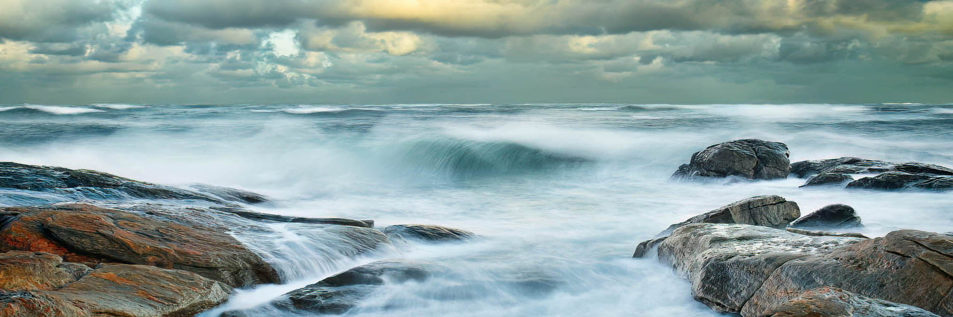 Ocean waves crashing against rocks with a cloudy sky.