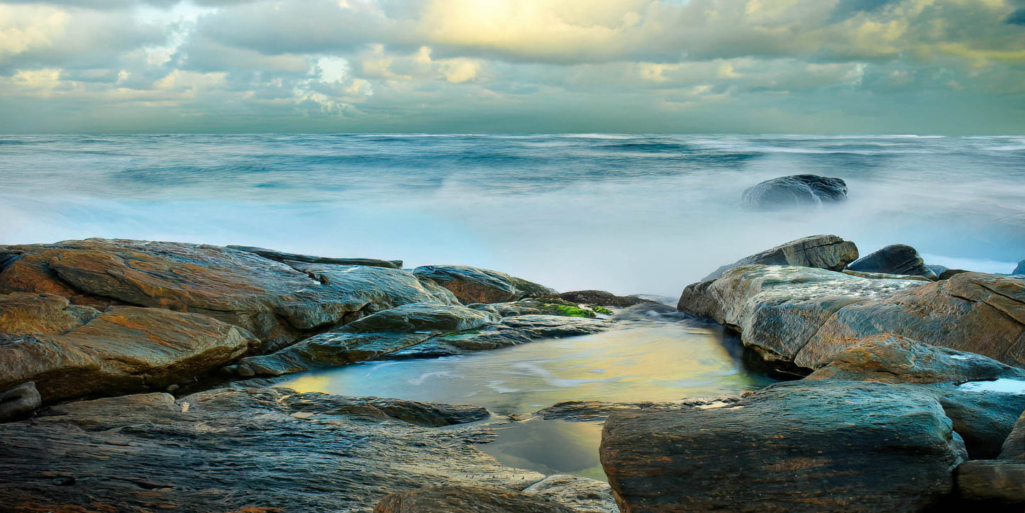 Rocks on a beach with ocean waves and cloudy sky