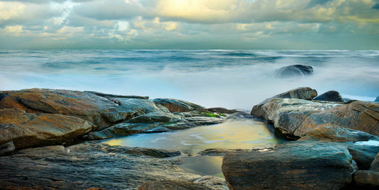 Rocks on a beach with ocean waves and cloudy sky