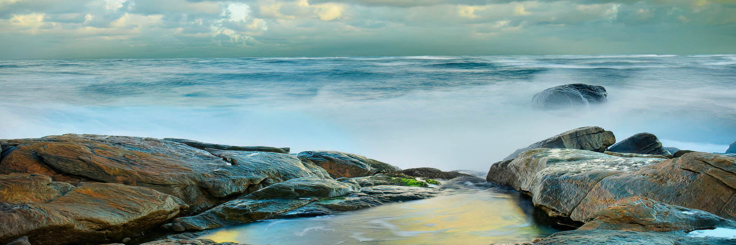 Rockpool by the ocean with a cloudy sky.