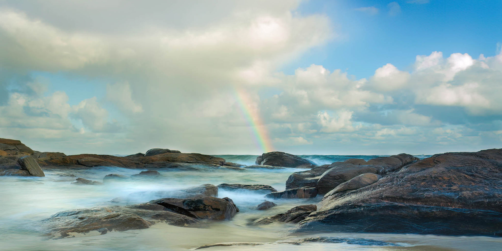 Rock plateau by the ocean at Redgate Beach, with a rainbow in the sky.