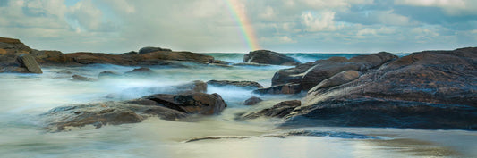 Rocks by the ocean with a rainbow in the background at Redgate Beach.