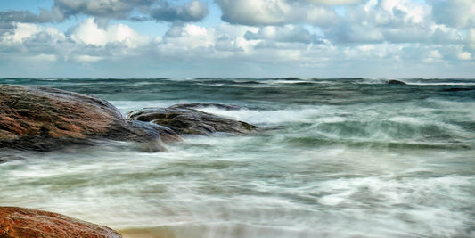 Long-exposure of ocean waves crashing against rocks with a cloudy sky at Redgate Beach.