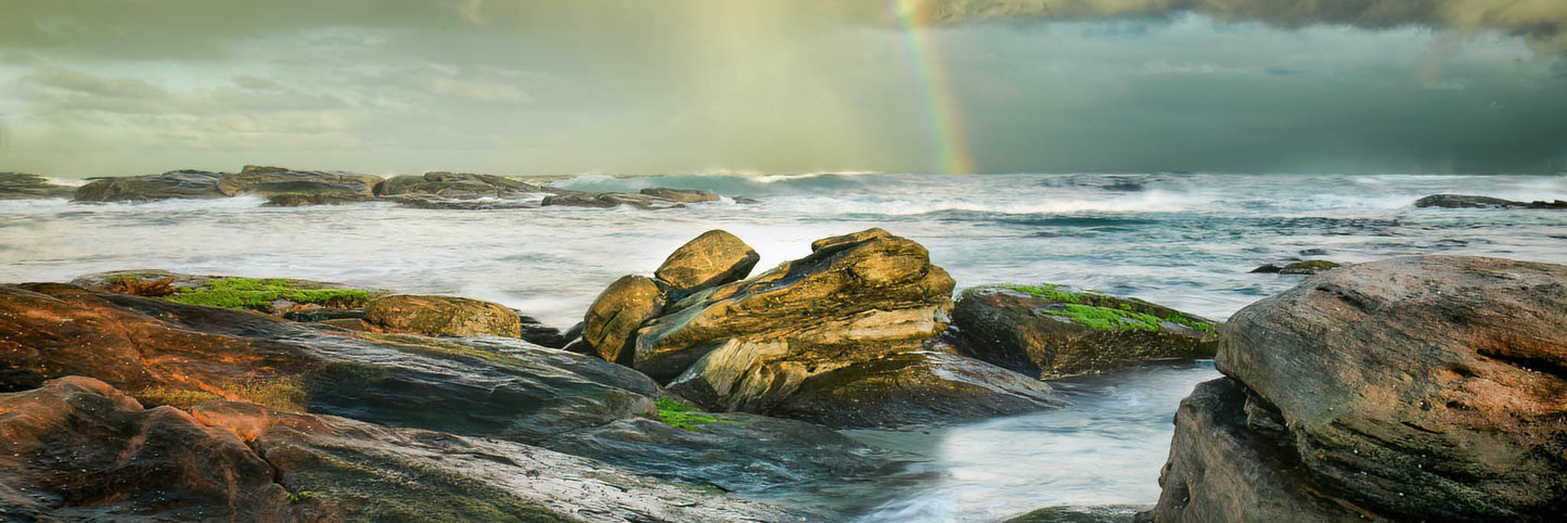 Rocks on a beach with a rainbow in the background