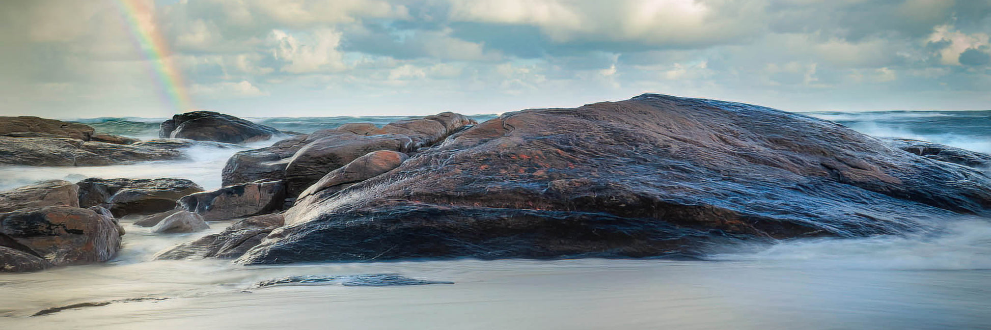 Rainbow on the horizon with rocks in foreground at Redgate Beach.