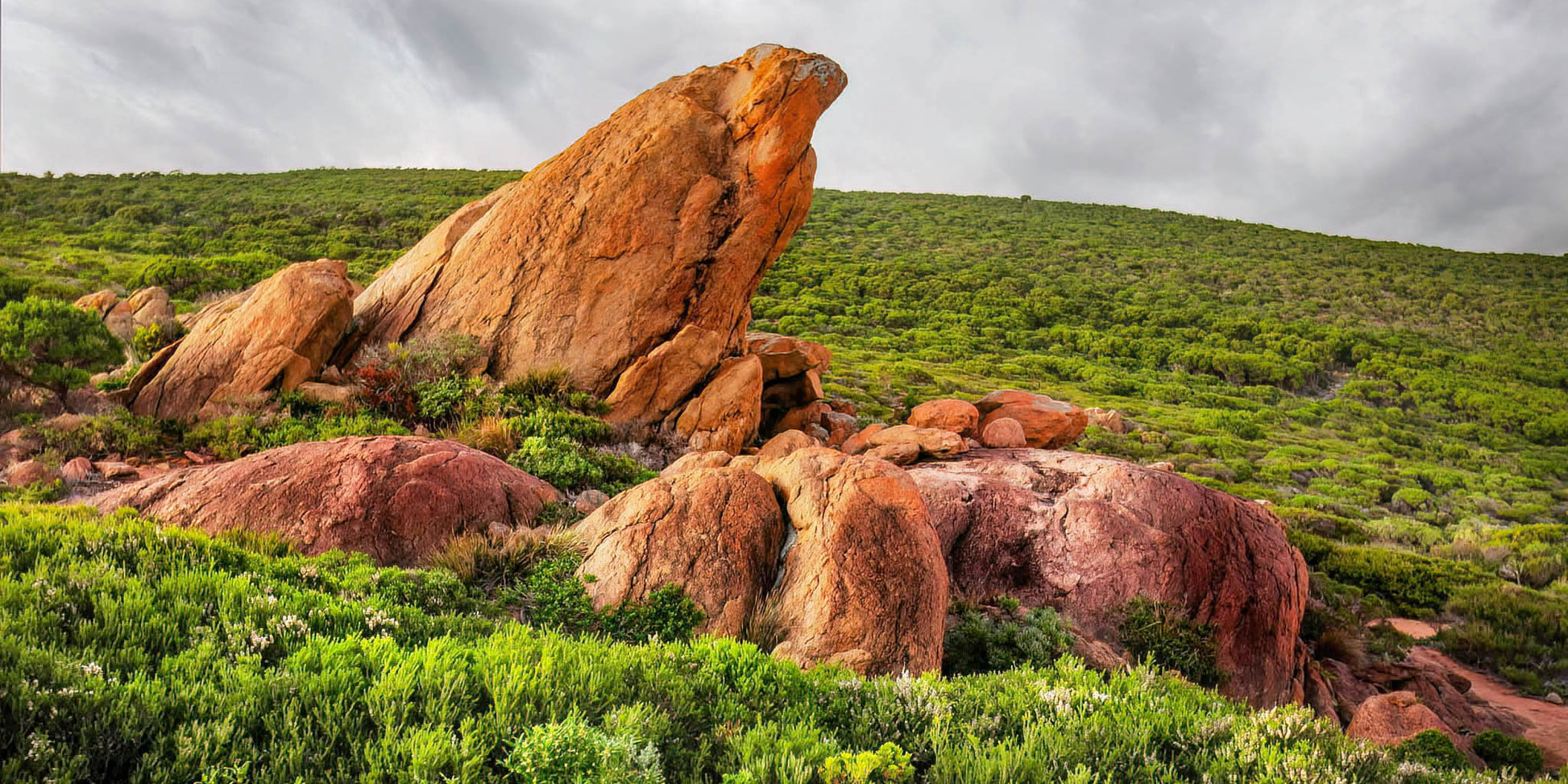 Large red rock formation in a grassy landscape with a cloudy sky.