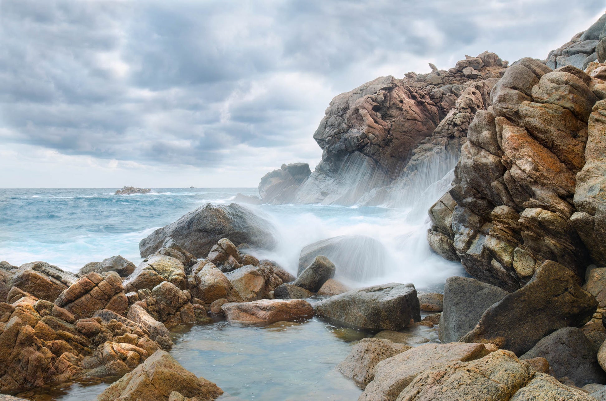 Moody seascape with long-exposure waves crashing on the rocks.