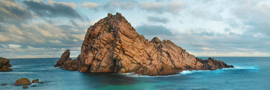Sugarloaf Rock in the middle of a blue ocean with a cloudy sky.