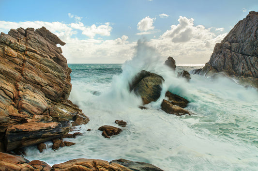 Sturdy granite rock formation holding strong against a surging swell.